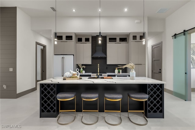 kitchen featuring a barn door, wall chimney range hood, a spacious island, high end white refrigerator, and pendant lighting