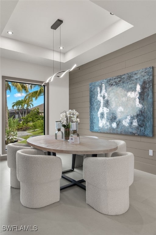 dining area with a raised ceiling and wood walls