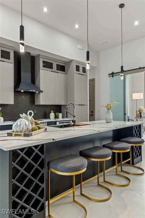 kitchen with wall chimney exhaust hood, a kitchen bar, hanging light fixtures, gray cabinets, and decorative backsplash