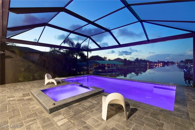 pool at dusk with a lanai, a water view, an in ground hot tub, and a patio