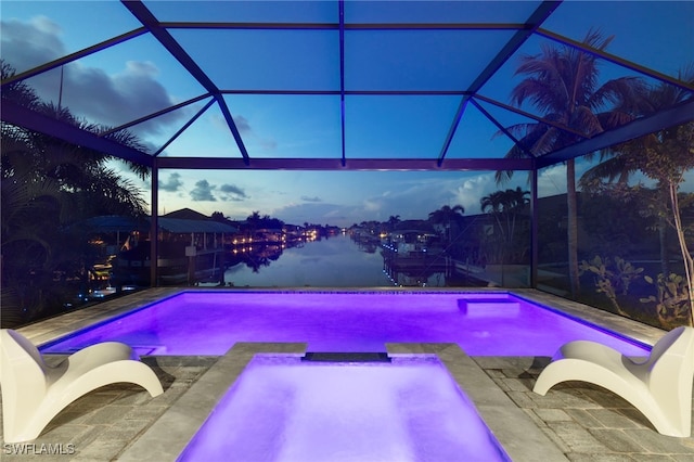 pool at dusk featuring glass enclosure and a patio area