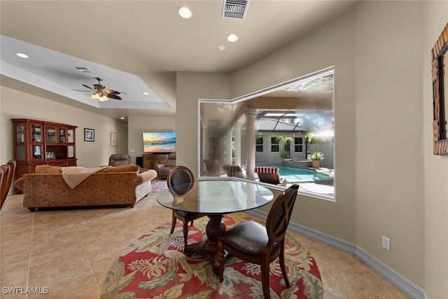 tiled dining space featuring a raised ceiling and ceiling fan