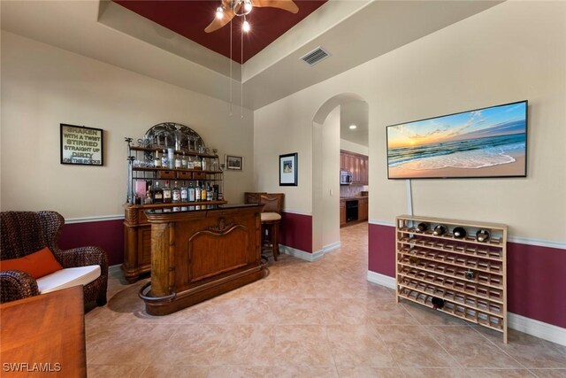 bar with a raised ceiling, ceiling fan, a towering ceiling, and light tile patterned floors