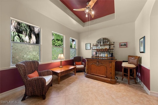 living area with ceiling fan, light tile patterned floors, a tray ceiling, and bar area