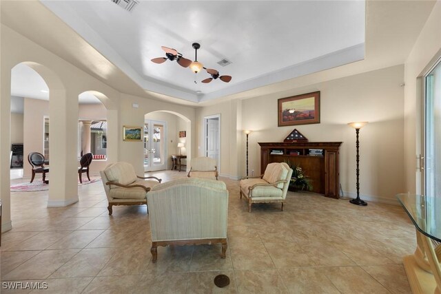 tiled living room with a tray ceiling, ceiling fan, and french doors