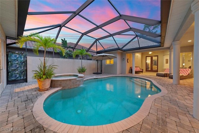 pool at dusk with a lanai, a patio area, and an in ground hot tub