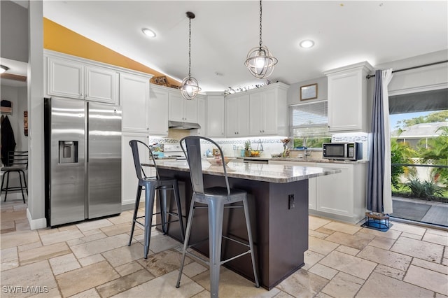 kitchen featuring pendant lighting, white cabinetry, stainless steel appliances, an island with sink, and vaulted ceiling