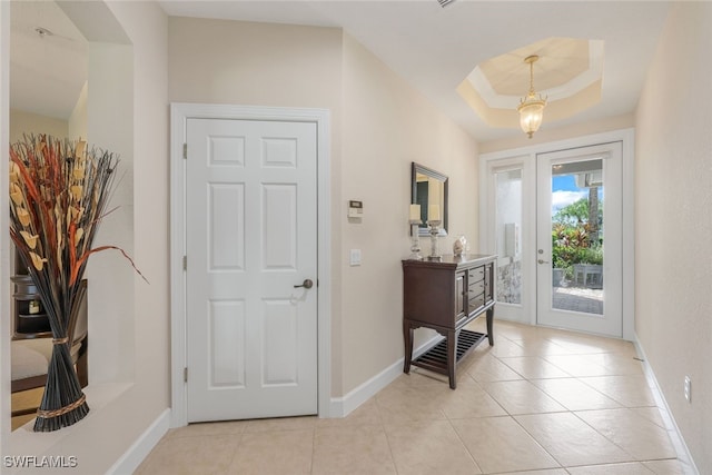 entryway with light tile patterned floors, a raised ceiling, and baseboards