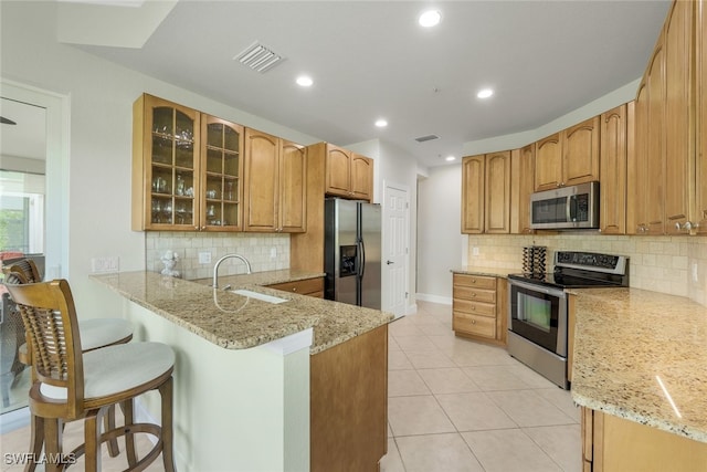 kitchen with a sink, light stone countertops, appliances with stainless steel finishes, and a peninsula