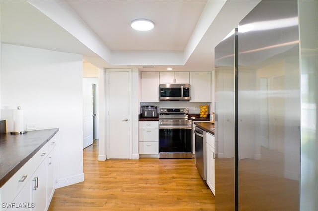 kitchen with a raised ceiling, light wood-type flooring, appliances with stainless steel finishes, and white cabinetry