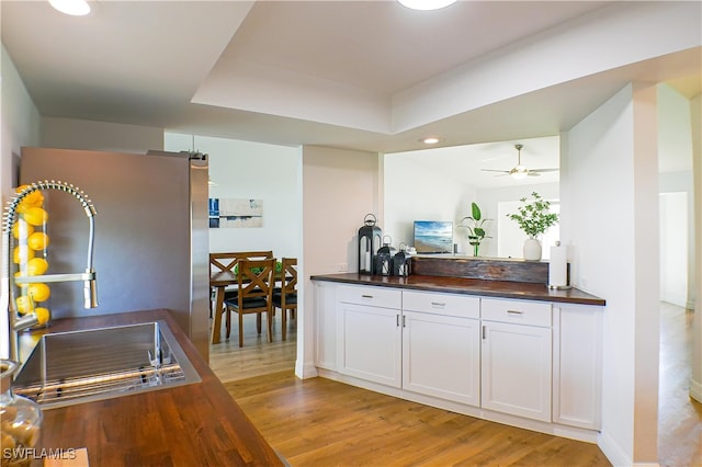 kitchen with light wood-type flooring, white cabinetry, wooden counters, sink, and ceiling fan