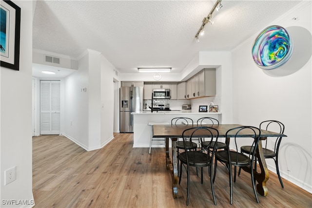 dining space featuring a textured ceiling, crown molding, hardwood / wood-style flooring, and track lighting