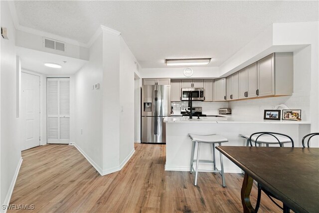 kitchen with gray cabinetry, backsplash, appliances with stainless steel finishes, kitchen peninsula, and light wood-type flooring