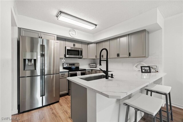 kitchen with a kitchen bar, kitchen peninsula, stainless steel appliances, and light hardwood / wood-style floors