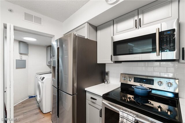 kitchen featuring a textured ceiling, light hardwood / wood-style flooring, backsplash, washer and dryer, and stainless steel appliances