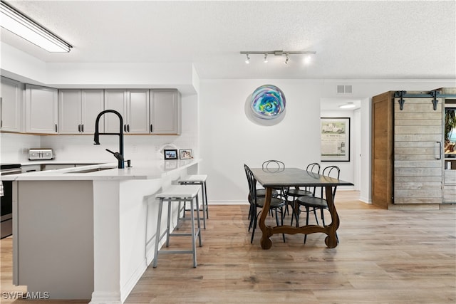 kitchen featuring a textured ceiling, gray cabinetry, a kitchen breakfast bar, kitchen peninsula, and light wood-type flooring