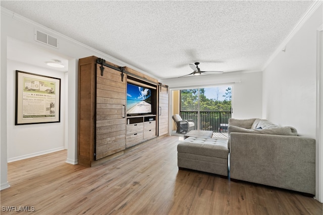 living room with a textured ceiling, crown molding, hardwood / wood-style flooring, a barn door, and ceiling fan