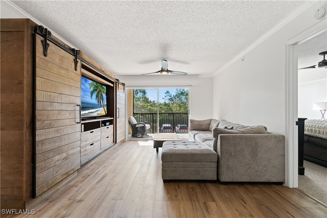 living room with ornamental molding, hardwood / wood-style floors, ceiling fan, and a barn door