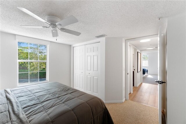 bedroom with a closet, ceiling fan, light hardwood / wood-style floors, and a textured ceiling