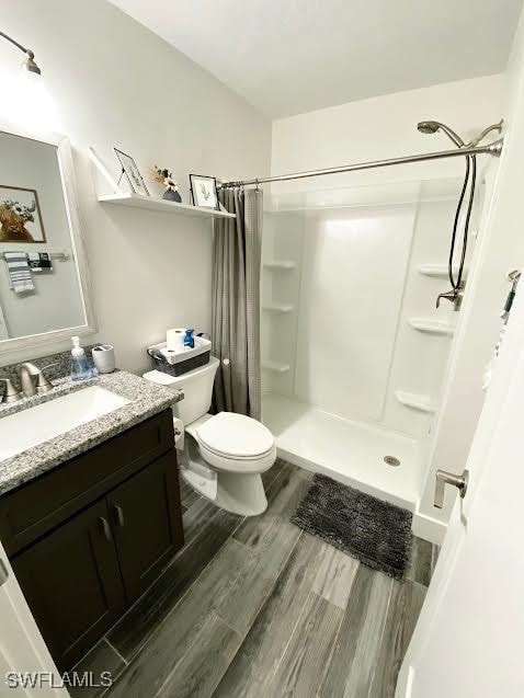 bathroom with wood-type flooring, vanity, toilet, and walk in shower