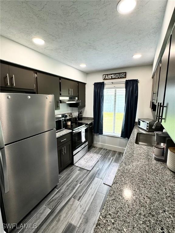 kitchen featuring a textured ceiling, stainless steel appliances, light hardwood / wood-style flooring, and dark stone countertops