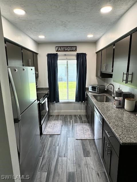 kitchen featuring sink, dark hardwood / wood-style floors, a textured ceiling, stone countertops, and appliances with stainless steel finishes