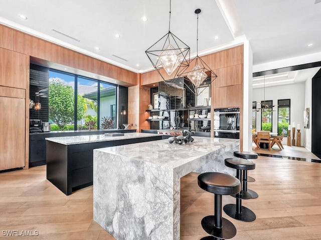 kitchen with a kitchen bar, a large island, decorative light fixtures, a chandelier, and light stone counters