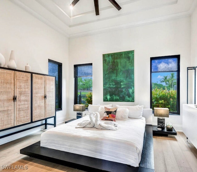 bedroom with ceiling fan, light wood-type flooring, and a towering ceiling