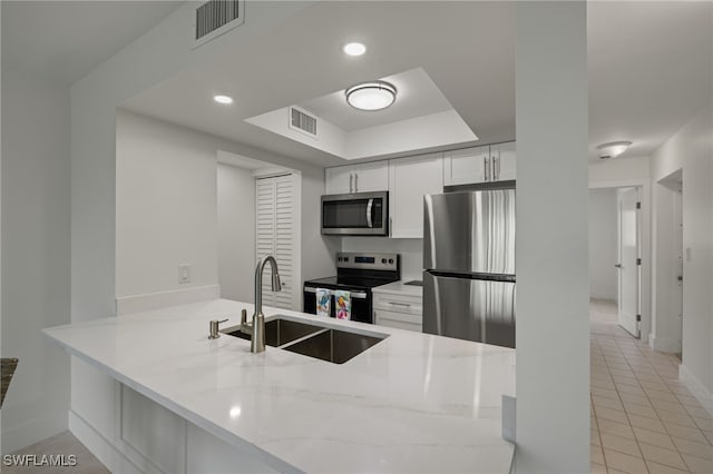 kitchen with light stone countertops, appliances with stainless steel finishes, kitchen peninsula, sink, and white cabinetry