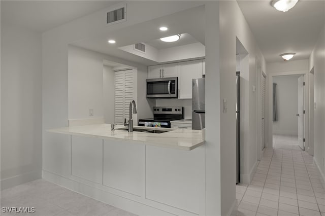 kitchen with light tile patterned floors, stainless steel appliances, sink, kitchen peninsula, and white cabinets