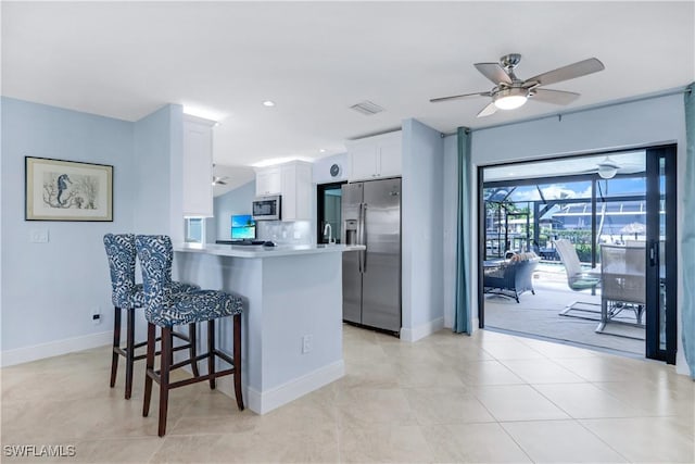 kitchen with kitchen peninsula, appliances with stainless steel finishes, backsplash, white cabinetry, and a breakfast bar area