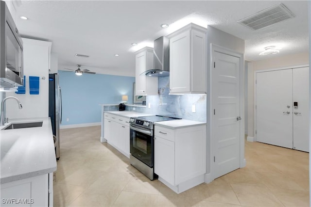 kitchen featuring sink, wall chimney exhaust hood, ceiling fan, white cabinetry, and stainless steel appliances