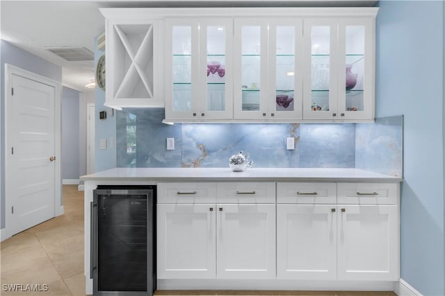 bar with tasteful backsplash, wine cooler, white cabinets, and light tile patterned floors