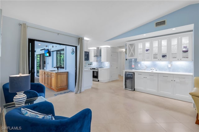 kitchen with decorative backsplash, vaulted ceiling, beverage cooler, stainless steel electric range oven, and white cabinetry