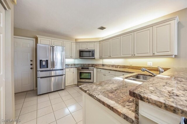 kitchen featuring sink, light tile patterned floors, light stone counters, white cabinetry, and stainless steel appliances