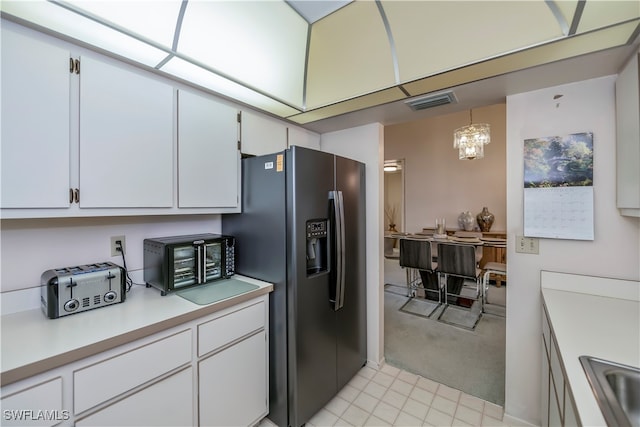 kitchen featuring stainless steel fridge, an inviting chandelier, white cabinetry, pendant lighting, and sink