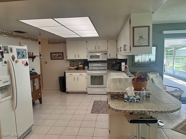 kitchen with a breakfast bar area, white appliances, kitchen peninsula, sink, and white cabinets