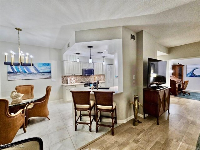 kitchen featuring tasteful backsplash, a chandelier, white cabinets, decorative light fixtures, and sink