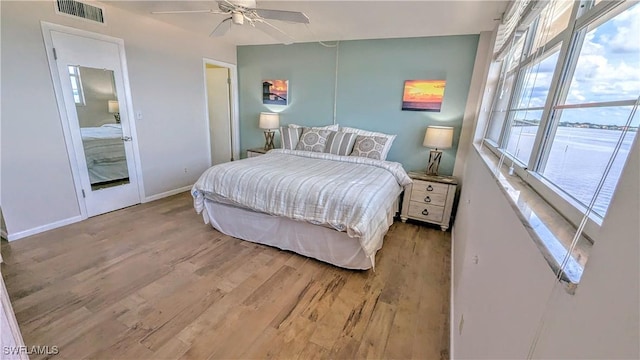 bedroom featuring a ceiling fan, visible vents, baseboards, and wood finished floors