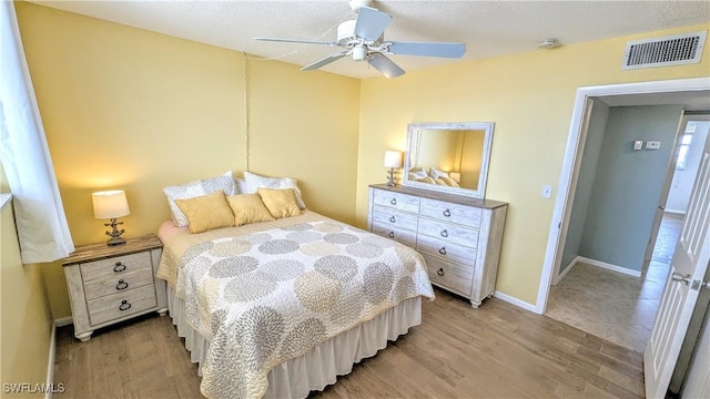 bedroom with ceiling fan, light wood finished floors, visible vents, and baseboards