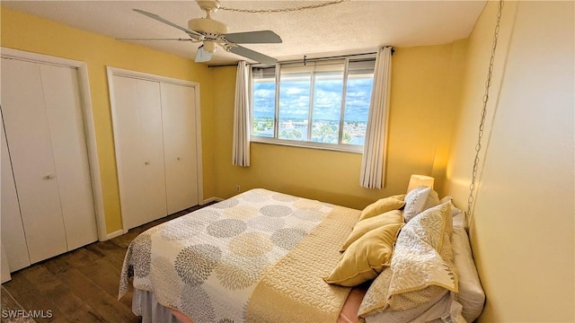 bedroom with multiple closets, dark wood-style flooring, ceiling fan, and a textured ceiling