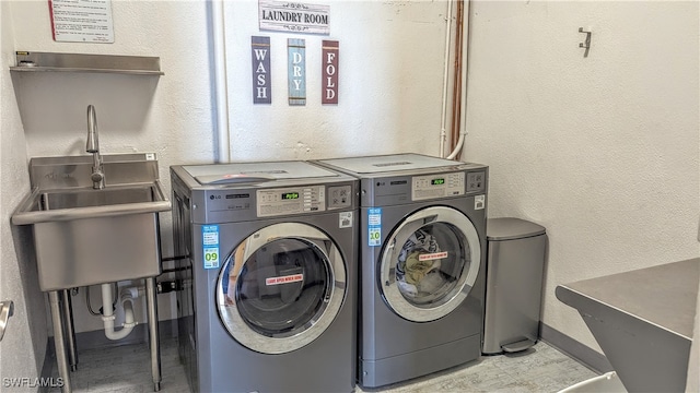 clothes washing area featuring a textured wall, washing machine and dryer, and a sink