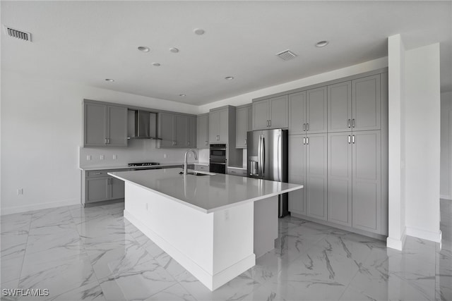 kitchen with a center island with sink, gray cabinets, wall chimney exhaust hood, and sink