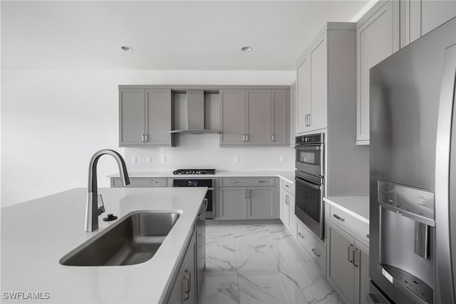 kitchen with gray cabinetry, sink, stainless steel appliances, and wall chimney range hood