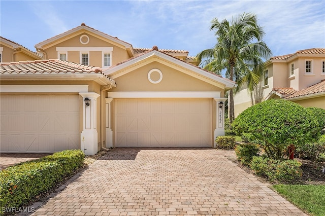 mediterranean / spanish-style house with a tiled roof, decorative driveway, an attached garage, and stucco siding