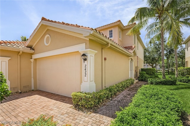 view of side of home with decorative driveway, a tiled roof, an attached garage, and stucco siding