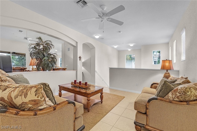 living area with a wealth of natural light, visible vents, a ceiling fan, arched walkways, and light tile patterned floors