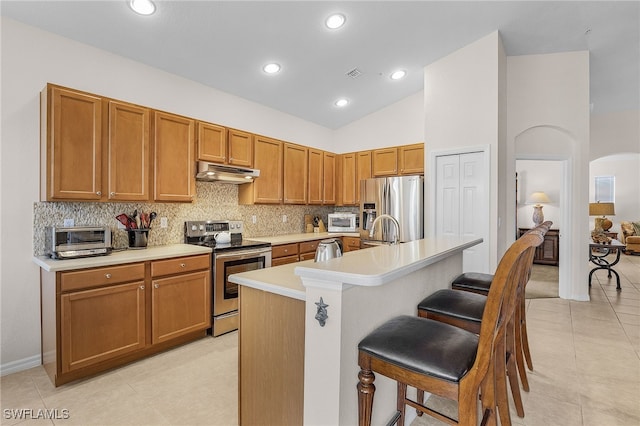 kitchen with a kitchen bar, light tile patterned floors, an island with sink, high vaulted ceiling, and appliances with stainless steel finishes