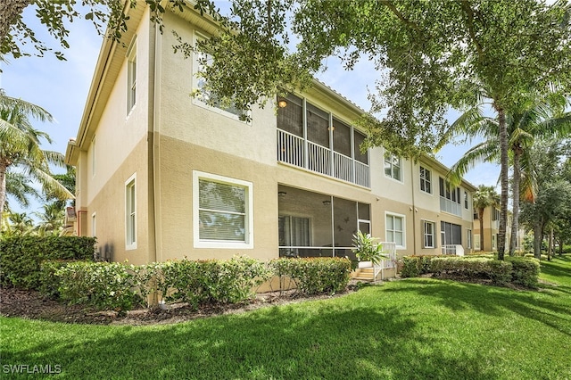 back of house featuring stucco siding, a yard, and a sunroom