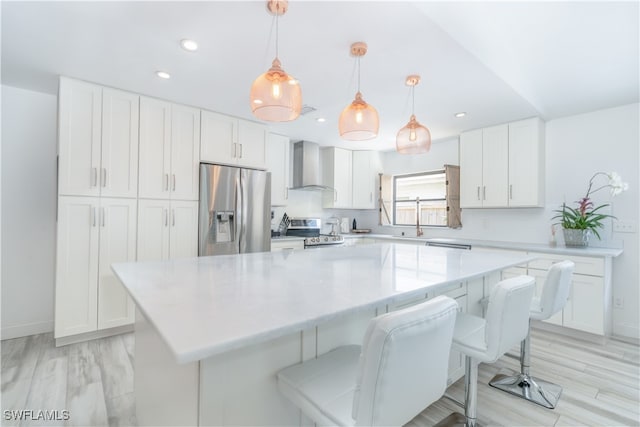 kitchen with pendant lighting, white cabinetry, a center island, appliances with stainless steel finishes, and wall chimney range hood